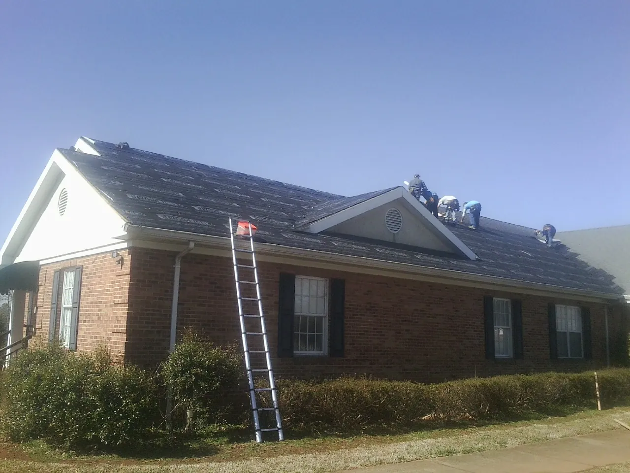 Crew tearing shingles off a brick ranch roof with a ladder set — Metal Roof Repair work by our crew in Armour