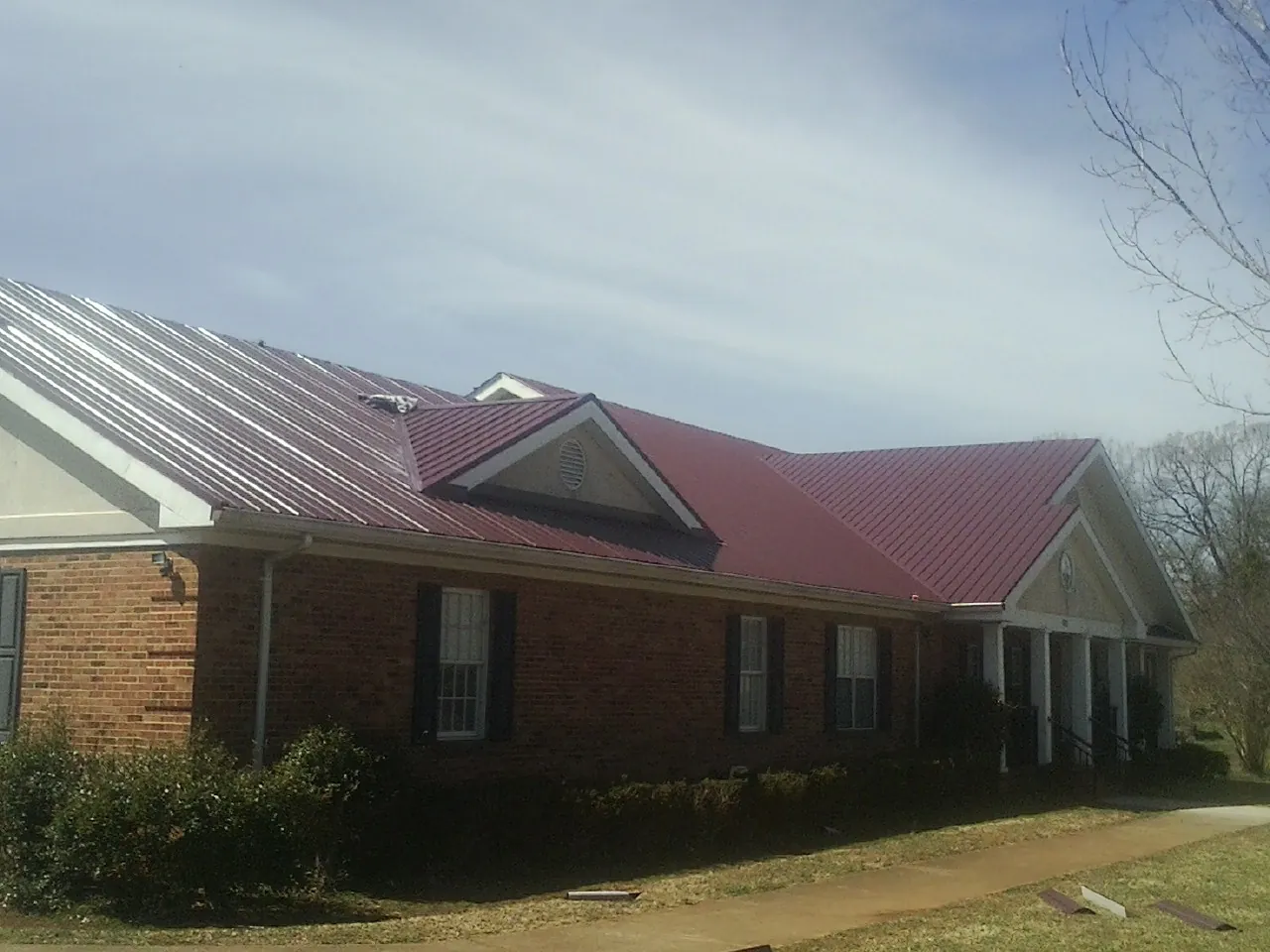 Red metal roof with gabled entries on a long brick building, from a Hail Damage Roof Repair job in Armour