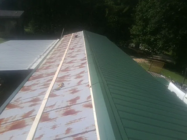 Old rusted panels beside newly installed green metal roofing — Wind Damage Roof Repair by Roofing Brothers in Armour
